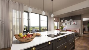 Una cucina moderna con un'isola grande, una ciotola di legno piena di frutta e vista sulla campagna.