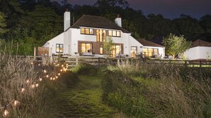 Una casa a due piani con facciata bianca, ampie finestre e una zona relax all'aperto.
