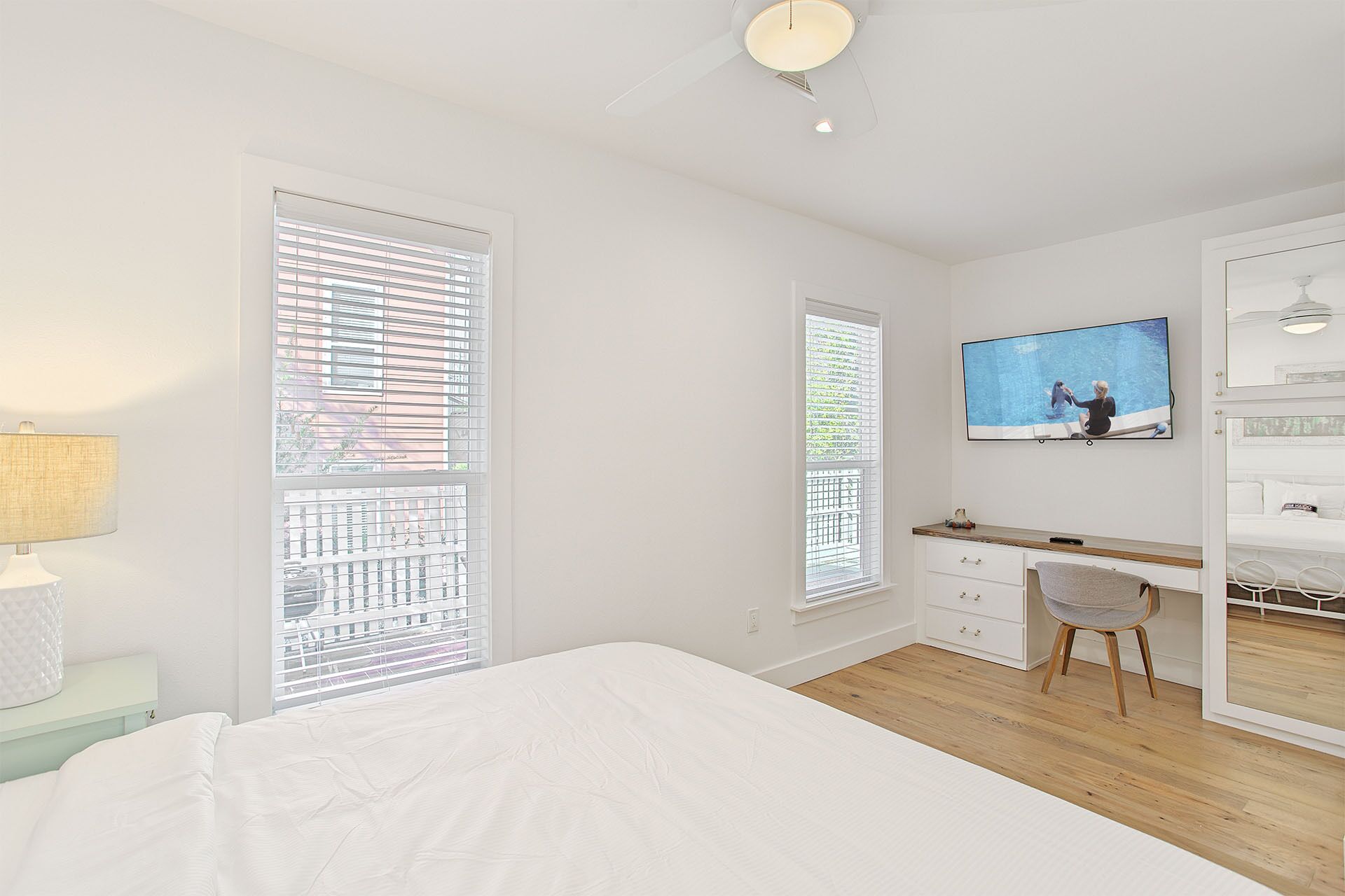 Une chambre à coucher comprenant un lit, un bureau, une chaise, un téléviseur et une fenêtre avec des stores.