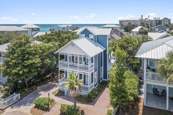 A coastal residential area with a prominent two-story house featuring a balcony and a view of the ocean.