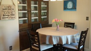 A dining area with a round table, chairs, a chandelier, a cabinet with glass doors, and a wall sign. - Historic Seneca Bungalow (Seneca)