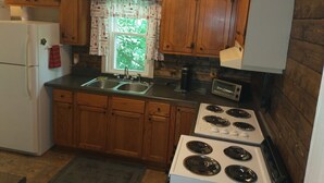 A kitchen with wooden cabinets, a white refrigerator, a double sink, and a stove. - Historic Seneca Bungalow (Seneca)