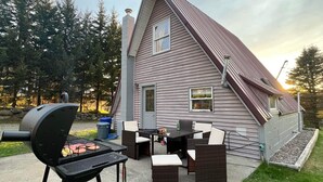 Een huis met een terras, inclusief een barbecue, tuinmeubilair en uitzicht op de omliggende bomen.