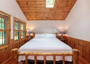 Une chambre avec un grand lit, une tête de lit en bois, deux tables de chevet avec des lampes et une lucarne.