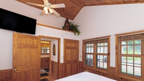 Ein Schlafzimmer mit Holzwandverkleidung, Deckenventilator, einem großen Bett und Fenstern mit Jalousien.