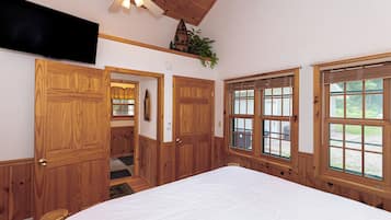 Une chambre avec des lambris en bois, un ventilateur de plafond, un grand lit et des fenêtres équipées de stores.