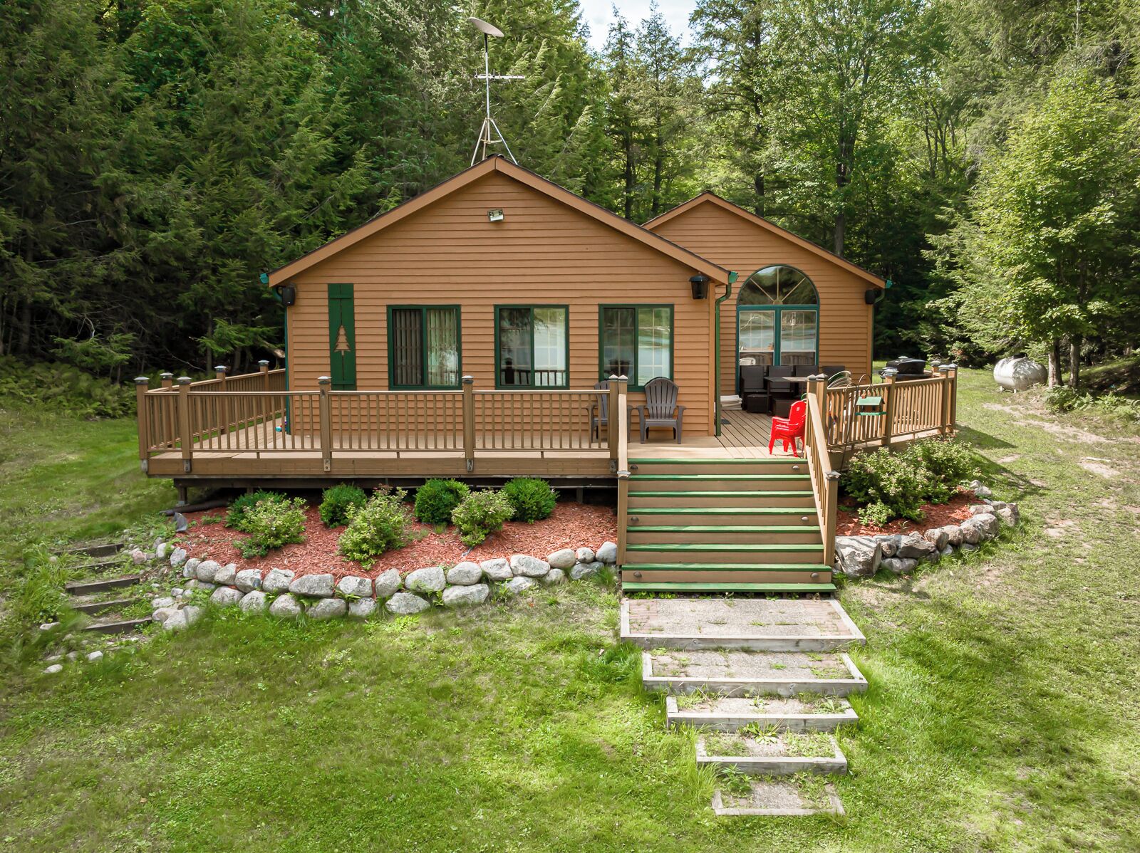 Une cabane dotée d’une terrasse en bois, d’un porche abrité et d’un petit espace extérieur aménagé pour s’asseoir.