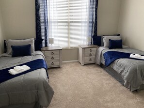 Une chambre avec deux lits, une table de chevet et une fenêtre avec des stores.