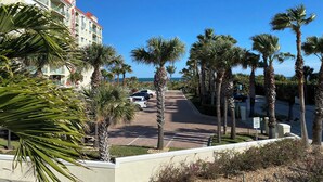 A hotel with a red roof and balconies, palm trees lining the street, and a clear view of the ocean.