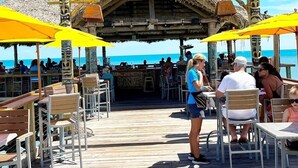 A tiki bar with a thatched roof and wooden deck, overlooking the ocean.