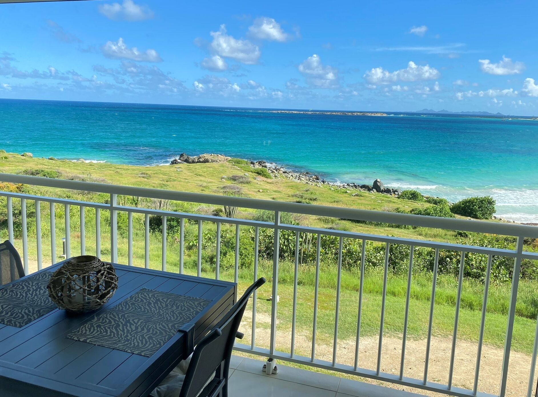A balcony with a view of the ocean, a table with a woven basket, and a chair.