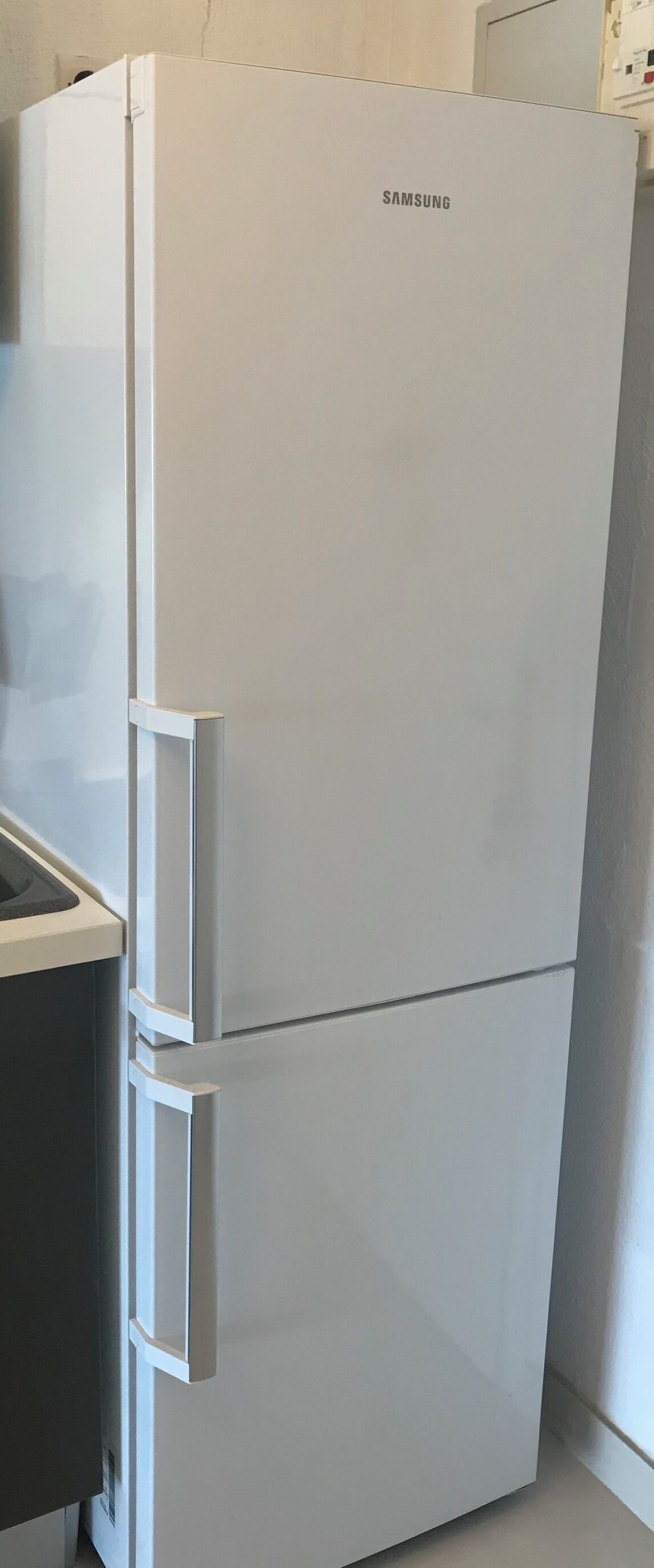 A white Samsung refrigerator with a freezer compartment on top and a refrigerator compartment below.