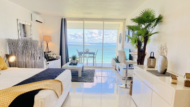 Une chambre d’hôtel moderne dotée d’un grand lit, d’un balcon avec vue sur la mer, d’un coin repas et d’une petite cuisine.