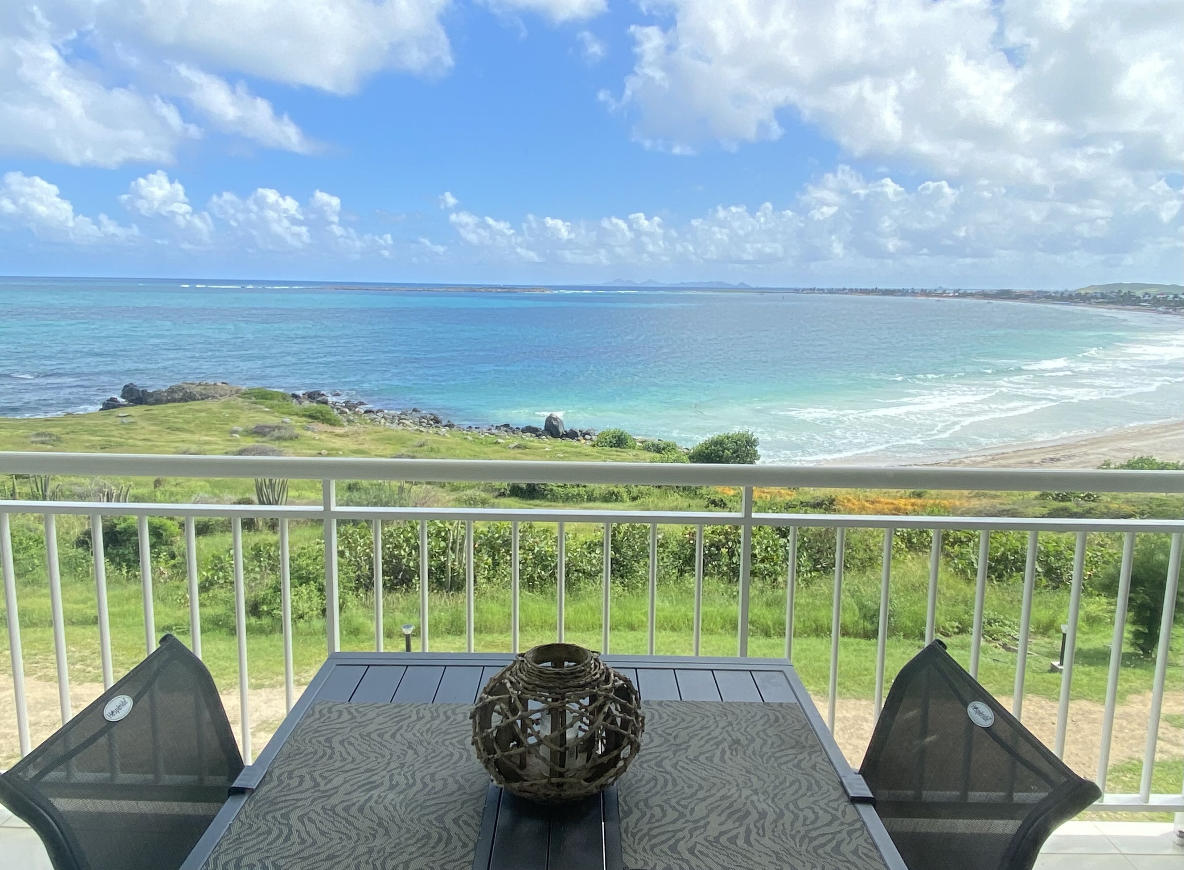 A balcony with a table and chairs, overlooking a beach and ocean.