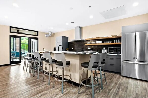 A modern kitchen with a central island, bar stools, stainless steel appliances, and a view of the outdoors.