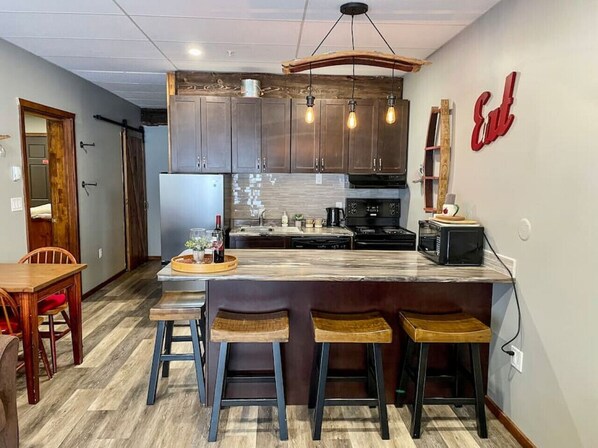A modern kitchen with a marble island, bar stools, and a hanging light fixture.