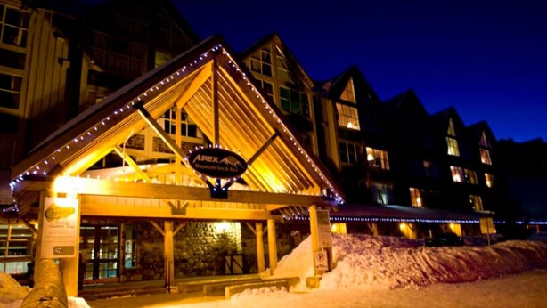 A lodge with a wooden exterior and a covered entrance, featuring a sign that reads "Apex Mountain & Ski." - Apex Mountain ~ Precision Palace ~ Apex Mountain Inn (Apex Mountain Resort)