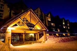 A lodge with a wooden exterior and a covered entrance, featuring a sign that reads "Apex Mountain & Ski."