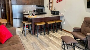 A modern kitchen with wooden cabinets, a central island with stools, and a red accent wall. - Apex Mountain ~ Precision Palace ~ Apex Mountain Inn (Apex Mountain Resort)