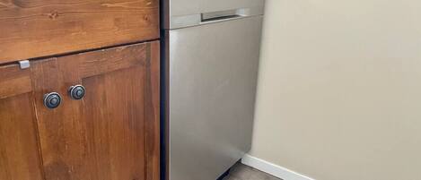 A kitchen with wooden cabinets, a stainless steel dishwasher, and a patterned floor.