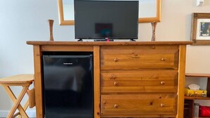 Un escritorio de madera compacto con refrigerador integrado, una pequeña unidad de cajones y un televisor encima.