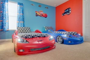 Un dormitorio infantil con dos camas con forma de coche y una pared azul decorada con motivos de coches.