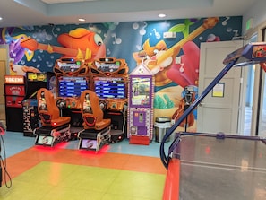 Una sala de juegos con máquinas de carreras, un cubo de basura y un mural en la pared.