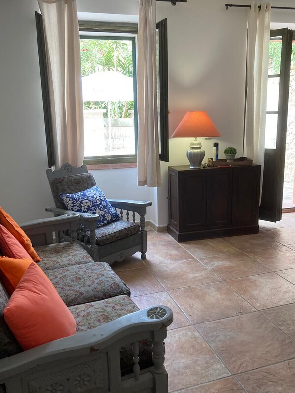 Un salon avec un canapé, une petite table sur laquelle se trouve une lampe, et une vue sur la verdure à l’extérieur.