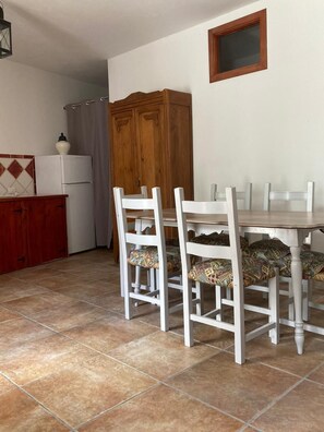 Un coin repas avec une table et des chaises blanches, un buffet en bois et un réfrigérateur.