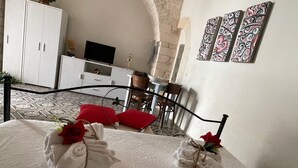 Une chambre d’hôtel avec une arche en pierre, un lit agrémenté de serviettes et de roses, un bureau avec une télévision et un coin repas.