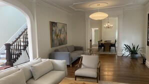 A spacious living room with a gray sofa, a wooden coffee table, and a gray armchair. A staircase with dark wooden railings is visible on the left.