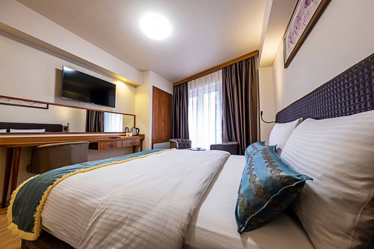 Hotelkamer met een bed, bureau met flatscreen televisie, stoel, kledingkast en raam met gordijnen.