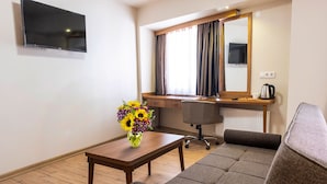 Ein modernes Wohnzimmer mit einer Couch, einem Holztisch, einer Vase mit Sonnenblumen, einem Schreibtisch mit Stuhl, einem Fernseher und einem Fenster mit Vorhängen.