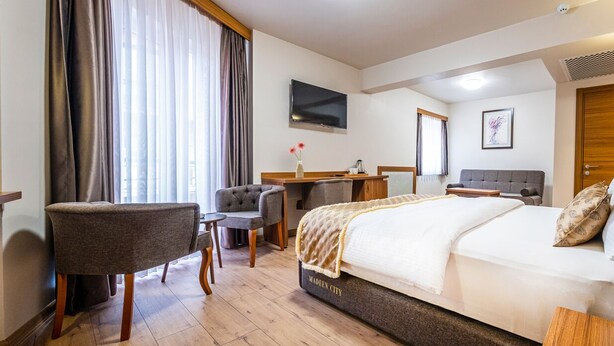 Ein Hotelzimmer mit Bett, Schreibtisch, Sessel, Fernseher und einem großen Fenster mit Vorhängen.