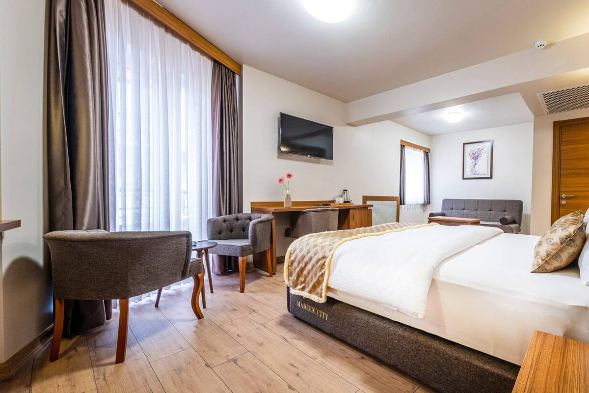 Hotelkamer met een bed, bureau, stoel, televisie en een groot raam met gordijnen.