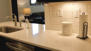 A kitchen with a stainless steel sink, a white countertop, a roll of paper towels, and a mug with text. - Ice Skating Suite 202 at Granby Dairy Suites (Granby)