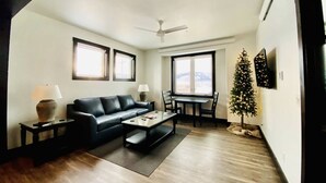 A modern living room with a black leather sofa, a coffee table, a dining table with chairs, a small Christmas tree, and a flat-screen TV mounted on the wall. - Ice Skating Suite 202 at Granby Dairy Suites (Granby)