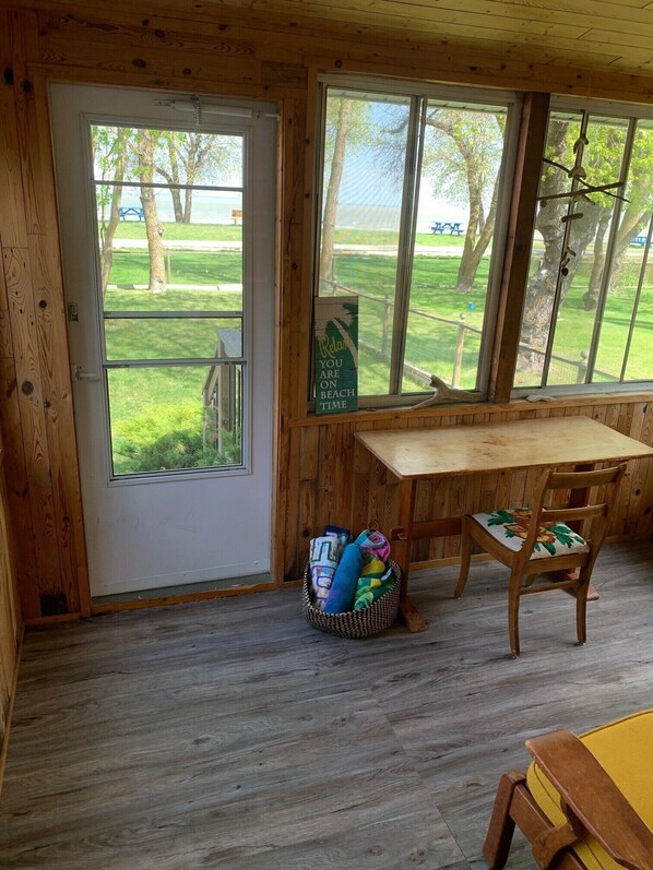 Une cabane en bois comprenant un coin repas, une fenêtre donnant sur une zone verdoyante et un panneau indiquant : « Détendez-vous, vous êtes en vacances à la plage. »