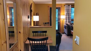 Un comedor con paredes de madera, una mesa y sillas. Hay una lámpara sobre la mesa y una ventana con cortinas.