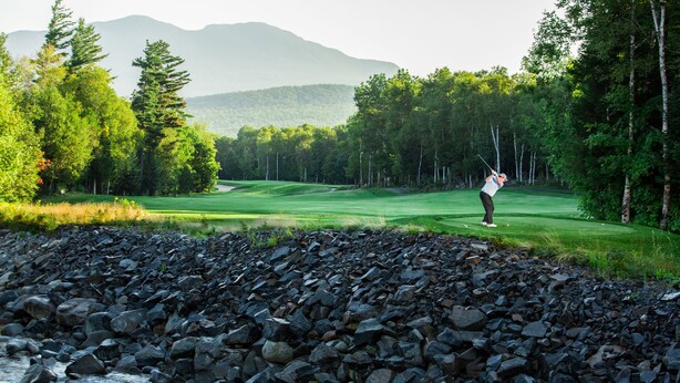 Un campo de golf con un primer plano rocoso y un río.