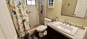 Un baño con inodoro, ducha, lavabo y espejo sobre el lavabo.
