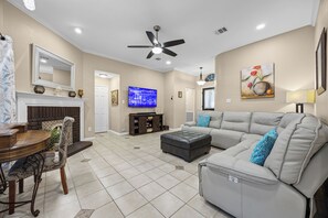 Una sala de estar con sofá seccional, televisor, chimenea y ventilador de techo.