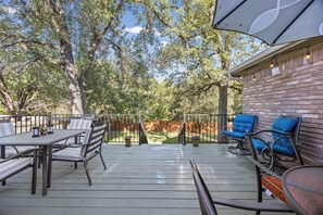An outdoor deck with a table and chairs, a brick wall, and a view of trees.