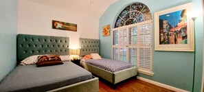 Un dormitorio con dos camas, una ventana con contraventanas y obras de arte en las paredes.