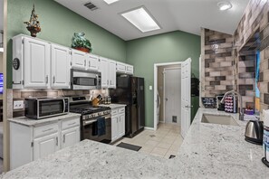 A modern kitchen with white cabinets, stainless steel appliances, and a green accent wall.