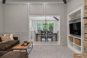 Relax in this stylish living room with a leather sofa, flat-screen TV, and dining area leading to a lush garden.