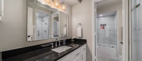 A modern bathroom with a black countertop, white cabinets, and a large mirror with lights.