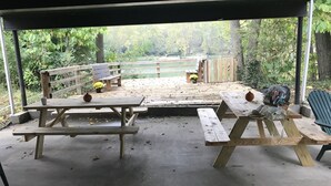 Ein überdachter Picknickbereich mit Holzbänken und Picknicktischen, umgeben von einem Holzzaun und Bäumen.