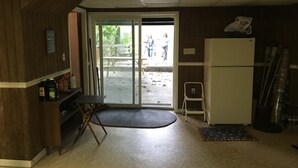 Ein Zimmer mit einer Holzwand, einem weißen Kühlschrank, einem kleinen Tisch und einer Bank vor der Tür.