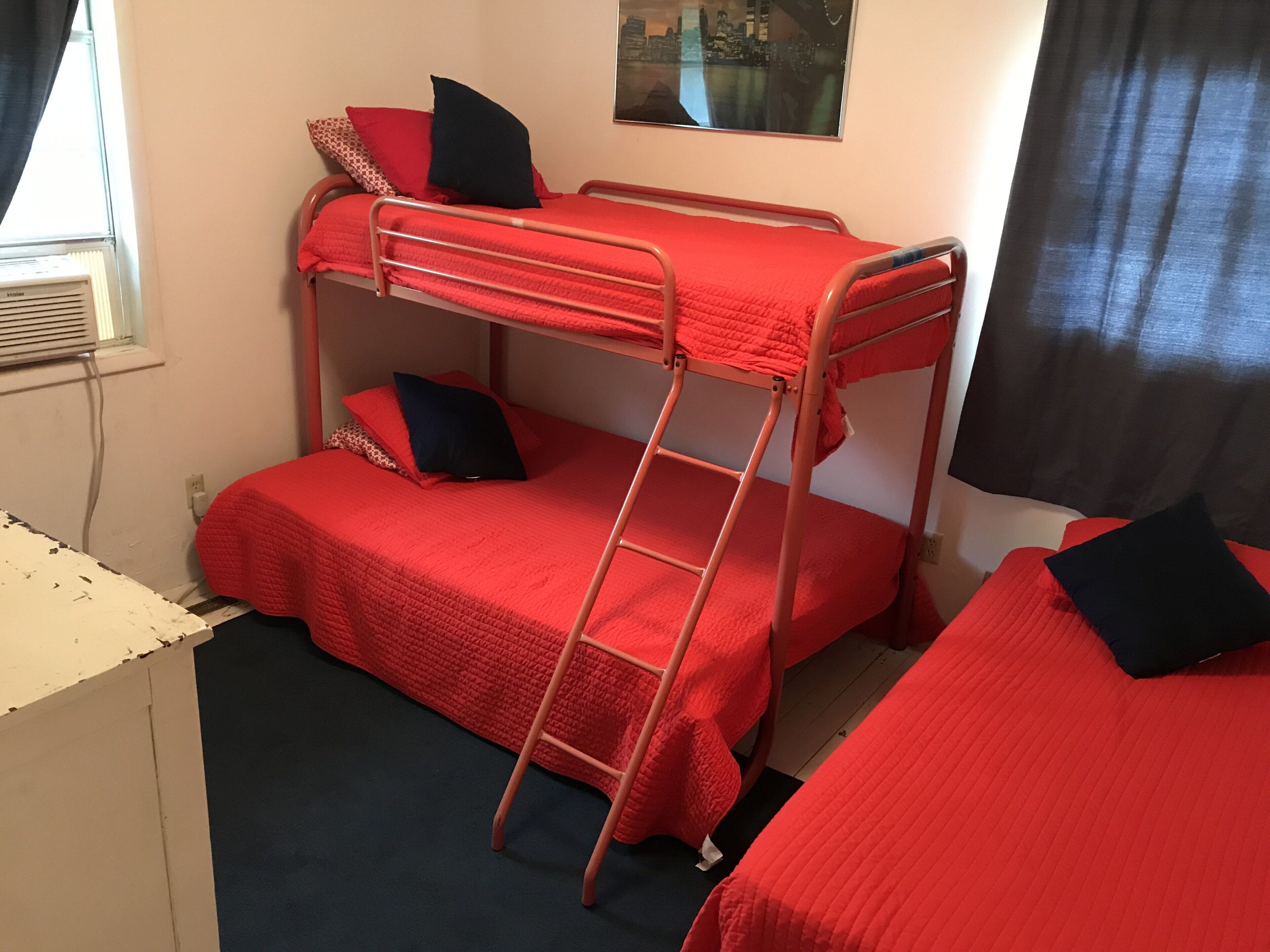 Een slaapkamer met een stapelbed, rode beddengoed en een ladder.